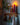 This image shows a shelf with hooks upon which sits a Greentree Petite Pillar candle in red, lit, among wintery items.