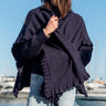 Woman wearing a dark blue poncho by a waterfront with boats in the background