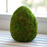 An artificial mossy egg decoration placed on a table, predominantly green in color.