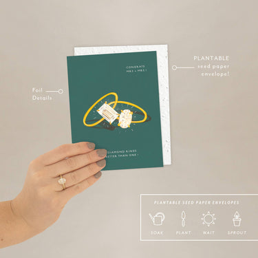 Hand holding a plantable seed paper envelope with a design of two interlocking rings on a green background.