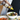 Person pouring sauce from a bottle onto a bowl of salad with various dishes on a table.