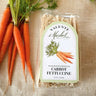Packaged carrot fettuccine with a Valente Market label next to fresh carrots on a textured surface.
