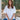 Woman with long brown hair seated wearing Mersea white pocket tee and blue jeans. Behind her are some trees.