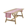 Wooden table with a pink and white patterned table runner on a white background