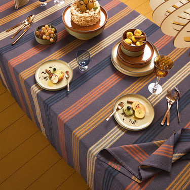 Dining table set with striped tablecloth, plates, glasses, and cutlery.