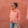 Woman wearing a pink striped shirt and sunglasses, standing against a textured red wall.