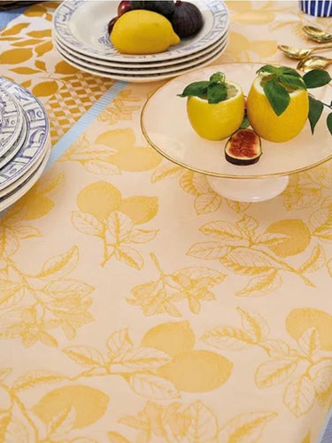 Dining table setting with lemons, figs, and decorative plates on a patterned tablecloth.