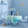 Dining table set with a light blue tablecloth, white chairs, and decorative items against a light blue wall.