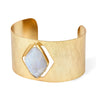 A wide, open cuff bracelet in brushed yellow gold with a large, irregular-shaped pale blue-gray stone set in the center, shown on a plain white background.