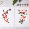 Two floral paintings on a gray surface with paintbrushes and color swatches.