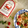 Valente Market fettuccine seasoning package with a bowl of pasta and shrimp on a textured surface