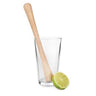 A natural wood muddler with a contoured handle, serrated base, and a lime slice placed next to it, all inside a cocktail glass.
